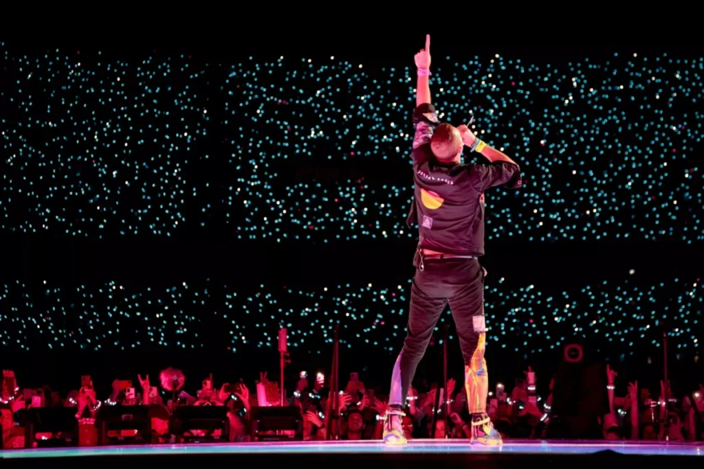 Coldplay se apresentando ao vivo durante a turnê, com público em êxtase e efeitos de luzes.