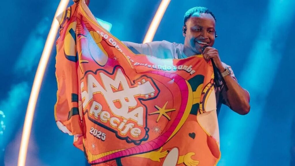Thiaguinho no palco durante o Samba Recife segurando bandeira do evento